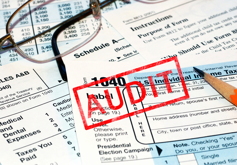 Red AUDIT stamp over IRS forms with glasses and pencil
