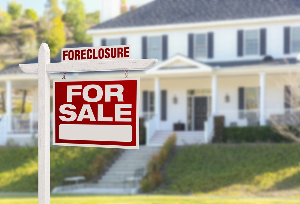 Foreclosure for sale sign outside of white 2-story home