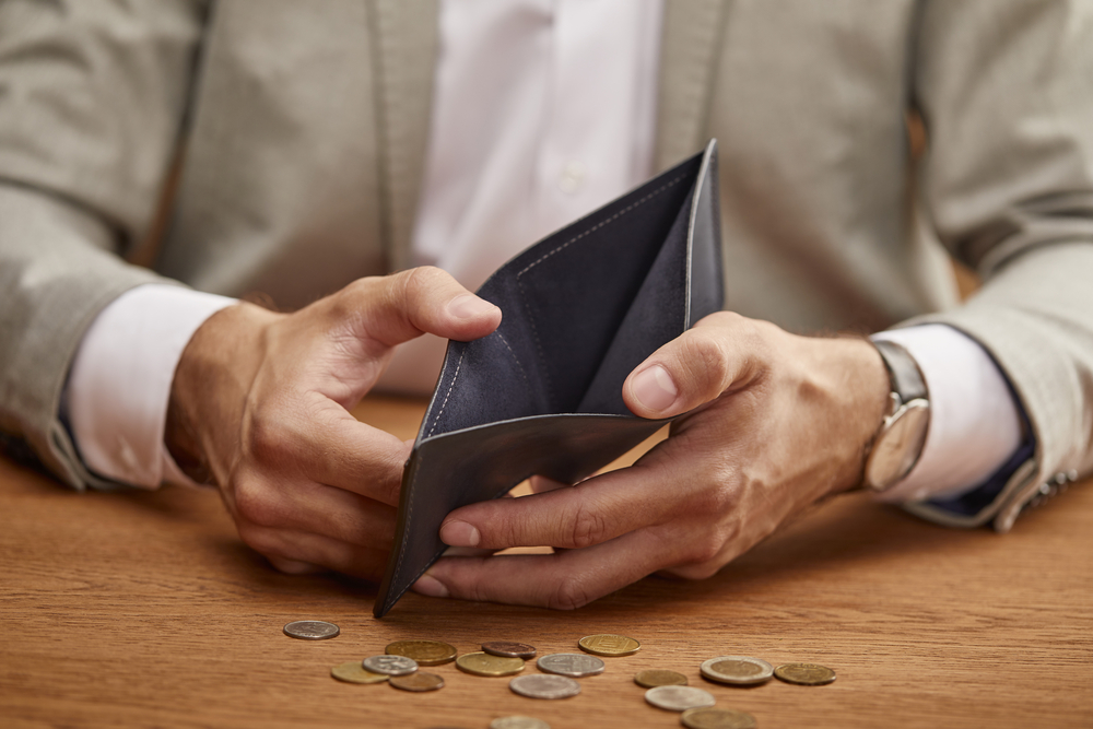 Man holding empty wallet open with a few coins scattered on table