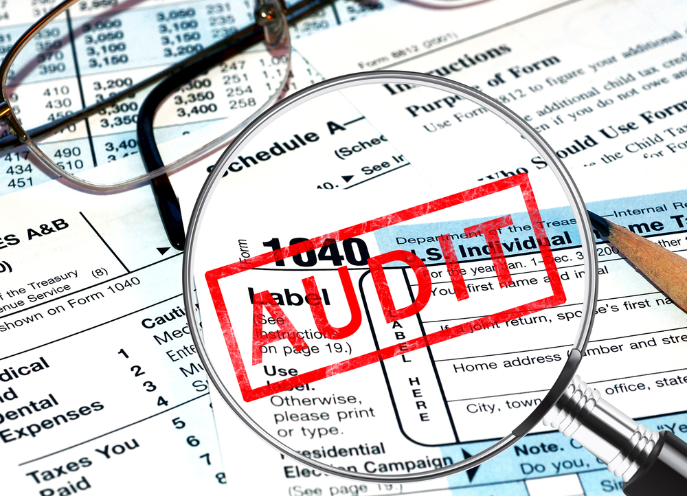 Magnifying glass and AUDIT stamp over tax papers