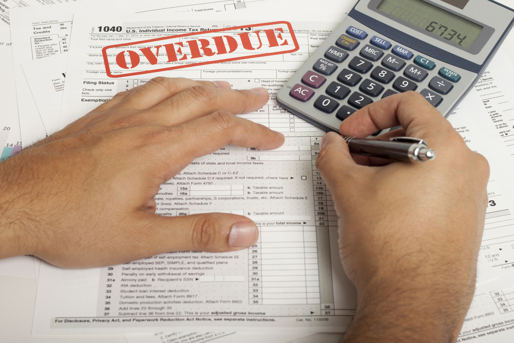 Man filling out overdue tax form using pen and calculator