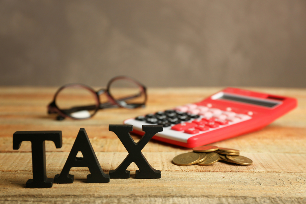Black letters spelling TAX on desk beside coins, calculator, and glasses