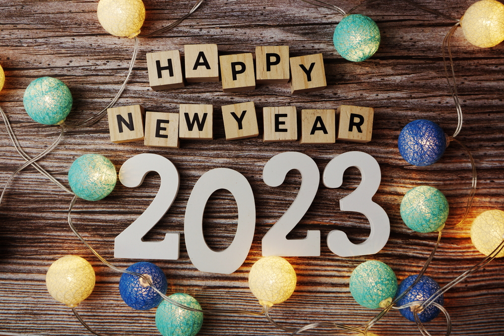Block letters spelling Happy New Year 2023 on wood surface surrounded by lights