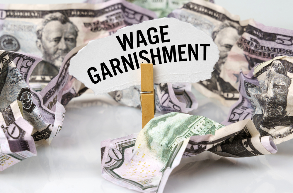 Wage garnishment sign on clip amid crumpled bills