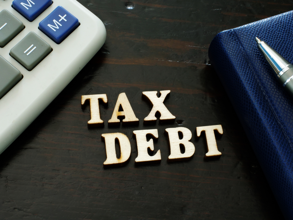 Tax Debt in wooden letters on desktop with calculator, book, and pen