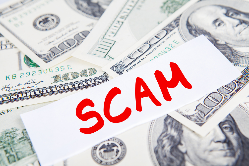 Scam written in red on paper atop pile of money