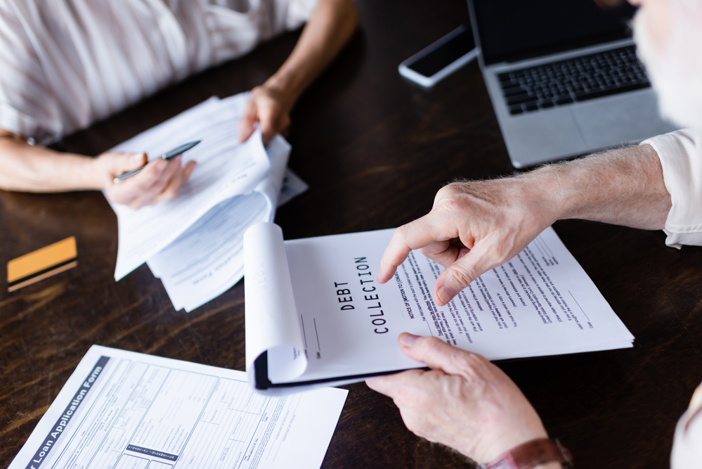 Close up of senior man pointing to debt collection papers on clipboard