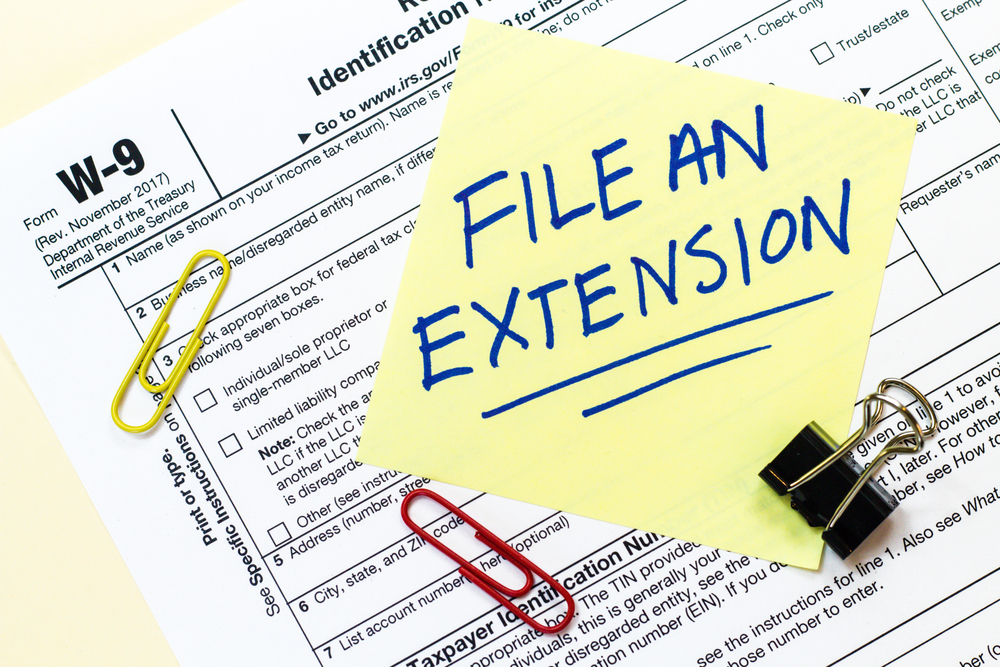 Sticky note reading File An Extension on top of W-9 tax form